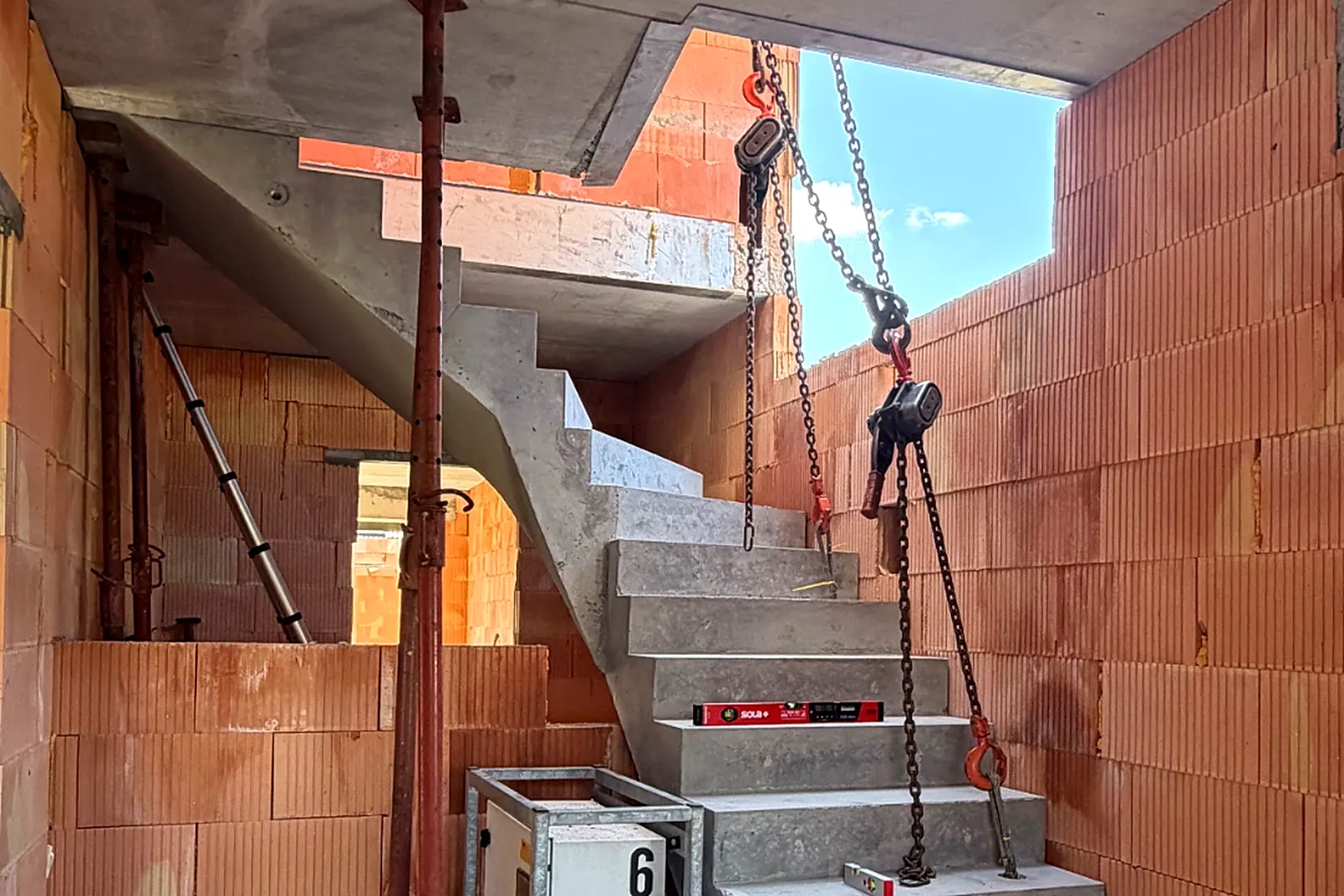 Prefab betontrap wordt met kettingtakels op zijn plaats gebracht in de ruwbouw van een woning
